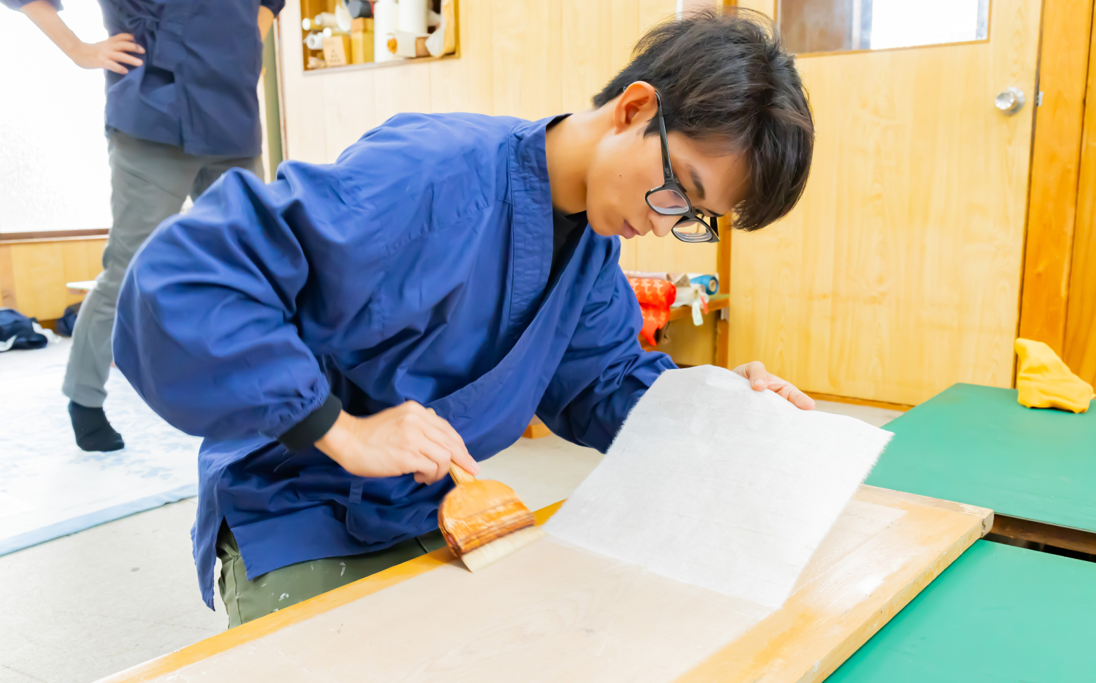和紙の上に刷毛をかけて作品を仕上げる職人の手元の様子