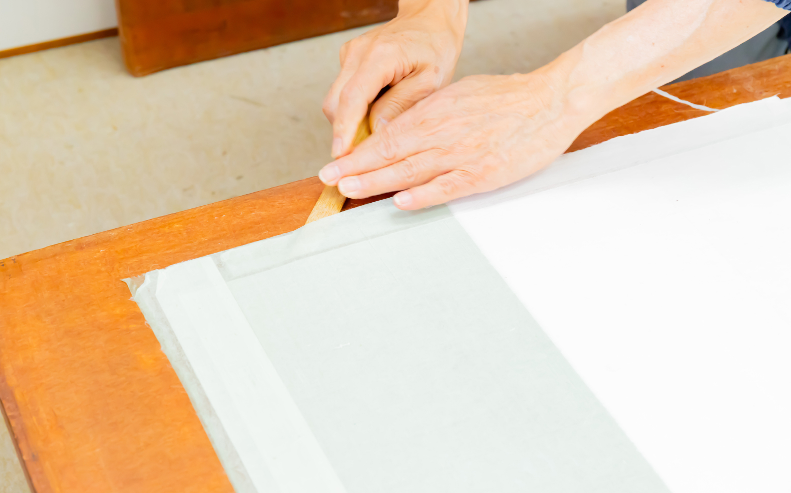 掛軸の作品を丁寧にめくりながら修復作業を行う職人の手元